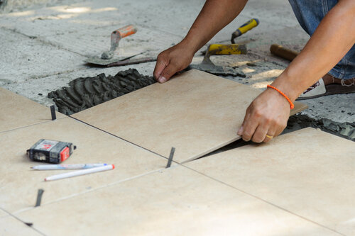 Tiler placing porcelain tile in position over adhesive. Floor tile installation
